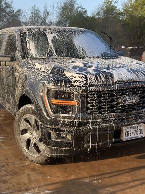 Black pickup truck covered in white foam during a car wash outdoors