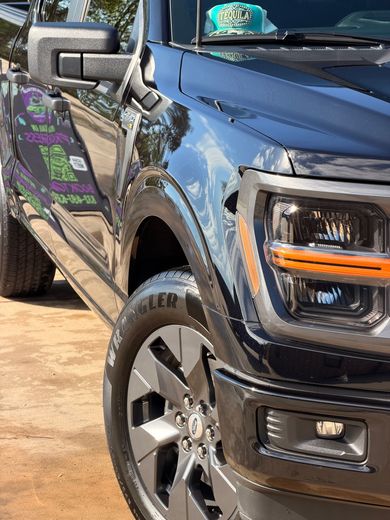 Blue pickup truck parked on a dirt surface, front and side view, with colorful custom door graphics.