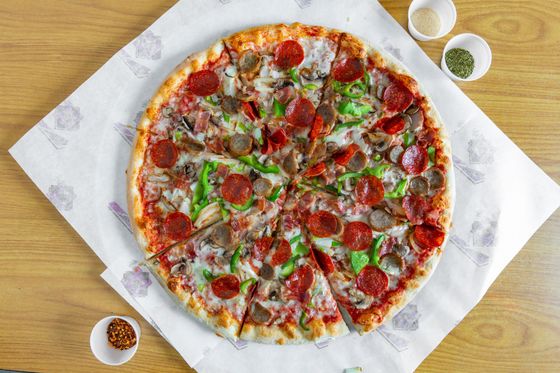 A pizza is sitting on a piece of paper on a wooden table.