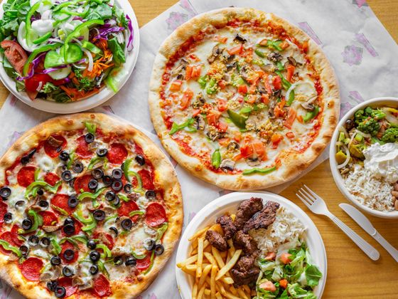 There are many different types of pizzas and plates of food on the table.