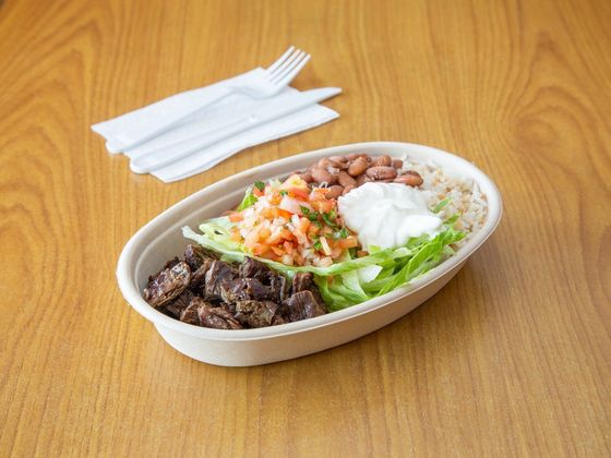 A bowl of food is sitting on a wooden table next to a napkin and fork.