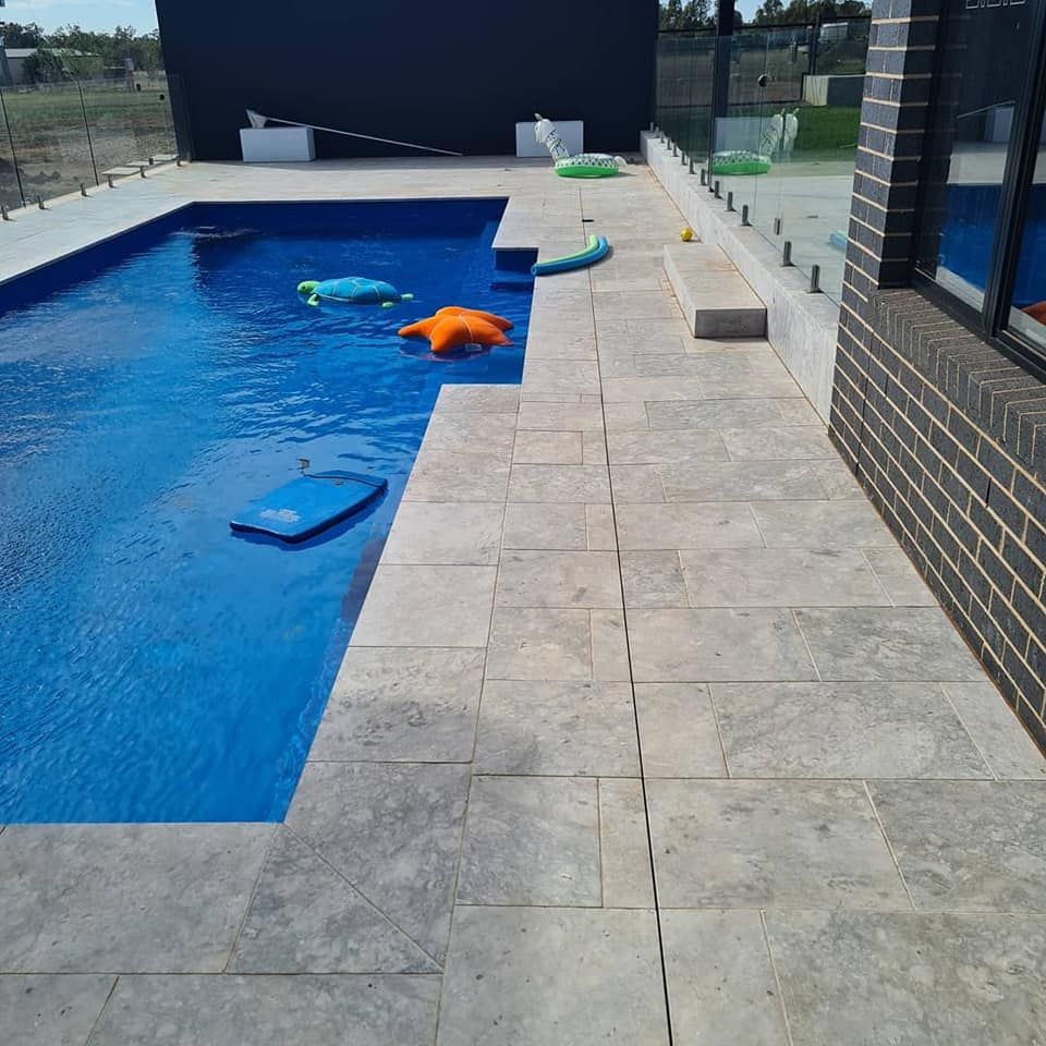 A Swimming Pool With a Brick Wall Surrounding It — Beaumont Plumbing in Glenfield Park, NSW