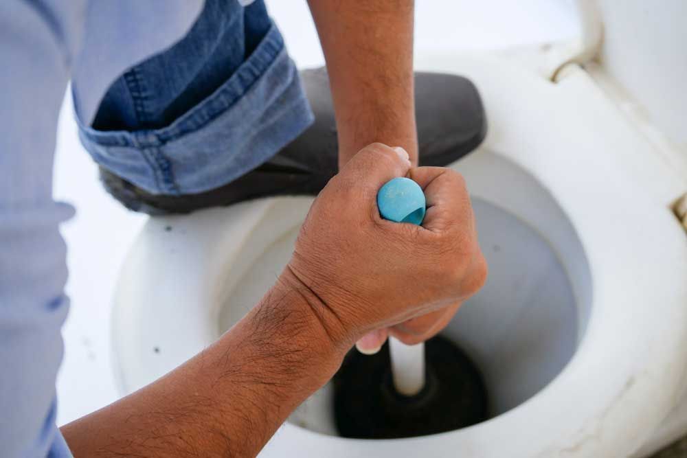 A Man is Using a Plunger to Unblock a Toilet — Beaumont Plumbing in Glenfield Park, NSW