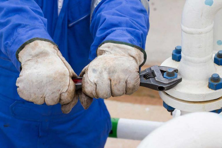 A Man Wearing Gloves is Working on a Pipe With a Wrench — Beaumont Plumbing in Glenfield Park, NSW