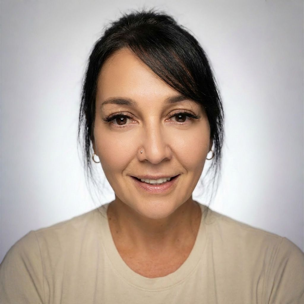 Woman with dark hair, smiling, wearing a teal sweater, in front of a neutral background.