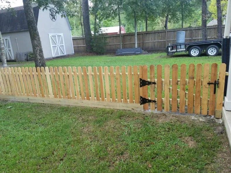 A wooden picket fence is sitting in the middle of a lush green yard.