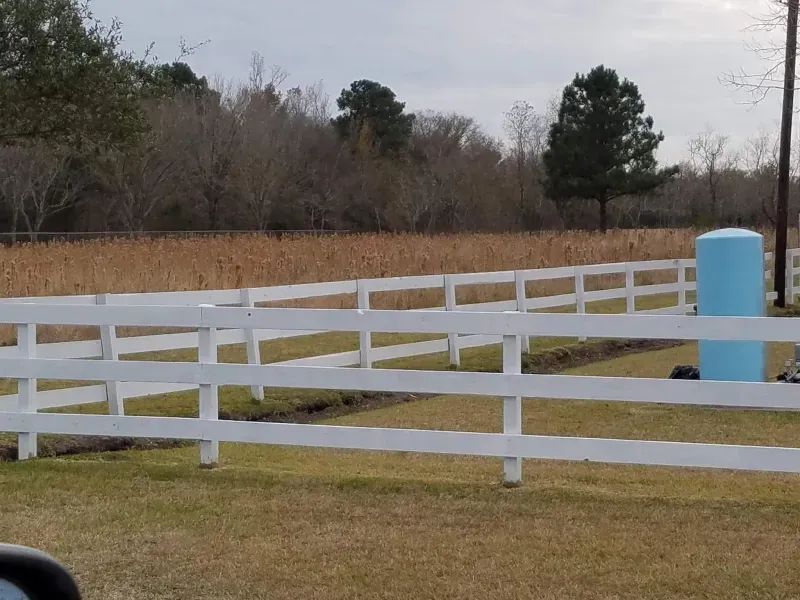 A white fence surrounds a grassy field with trees in the background