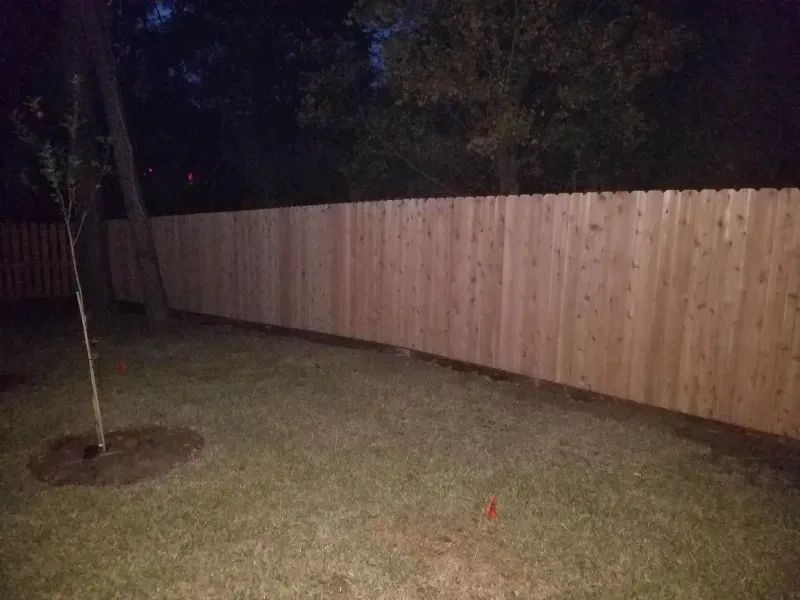 There is a wooden fence in the backyard at night.