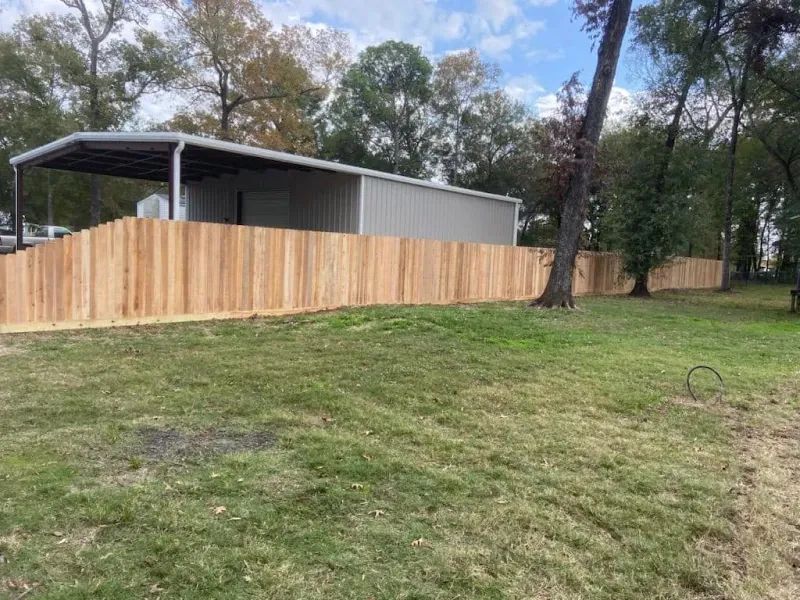 A wooden fence surrounds a shed in a grassy field.