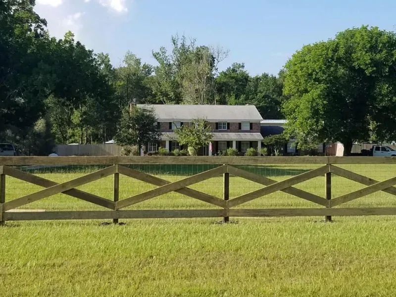 A wooden fence surrounds a grassy field in front of a house.