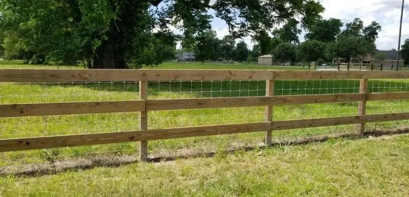 A wooden fence surrounds a grassy field with a tree in the background.