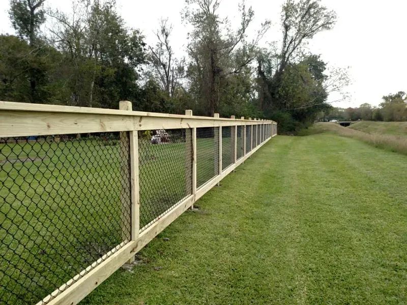 A wooden chain link fence surrounds a lush green field