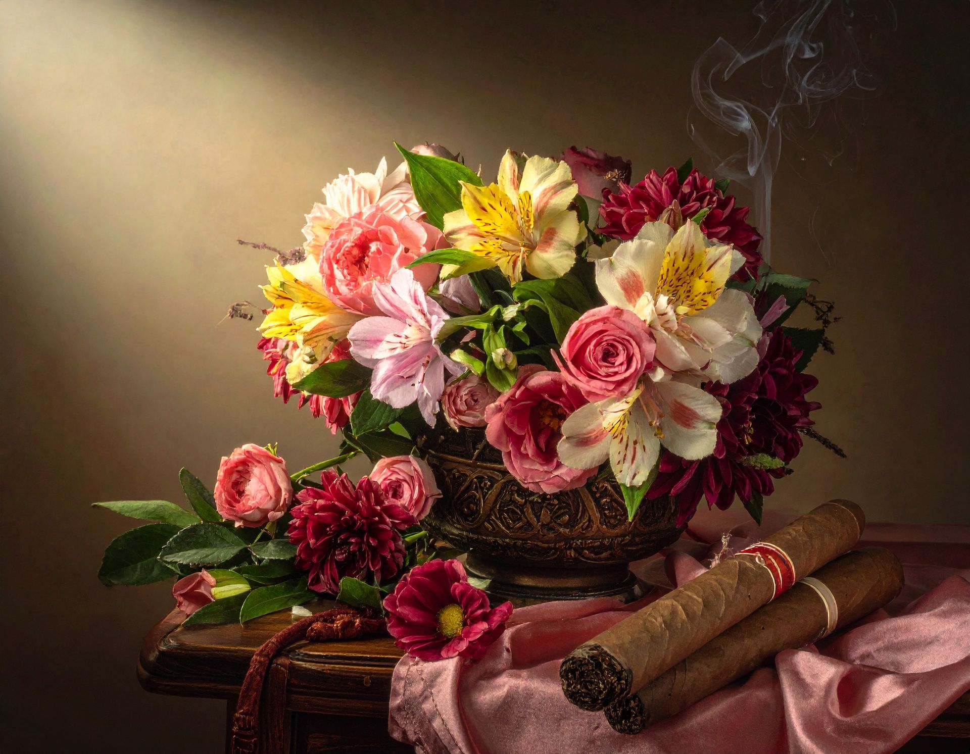 Bouquet of colorful flowers in ornate bowl, with lit cigars on pink cloth. Smoke rises.