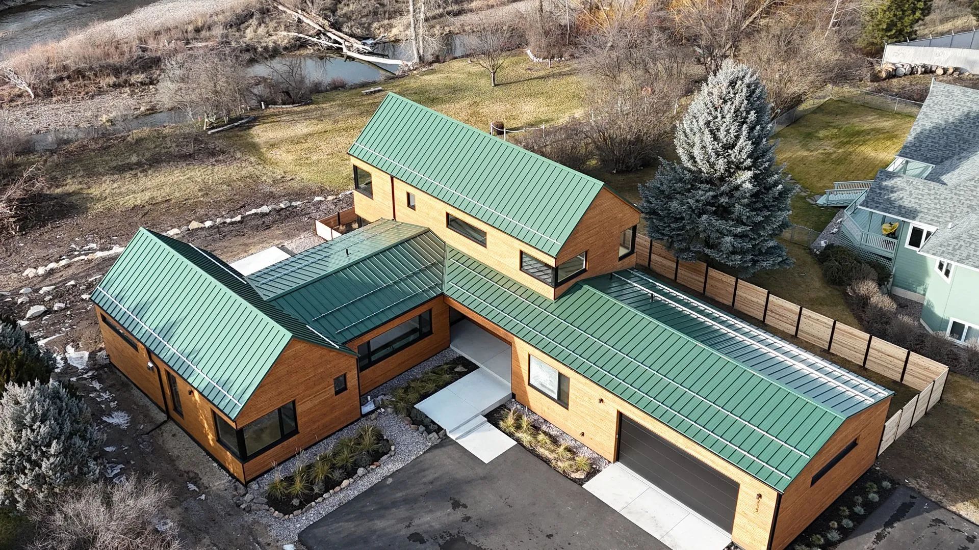 Aerial view of a modern house with green metal roofs and tan walls in a rural setting.
