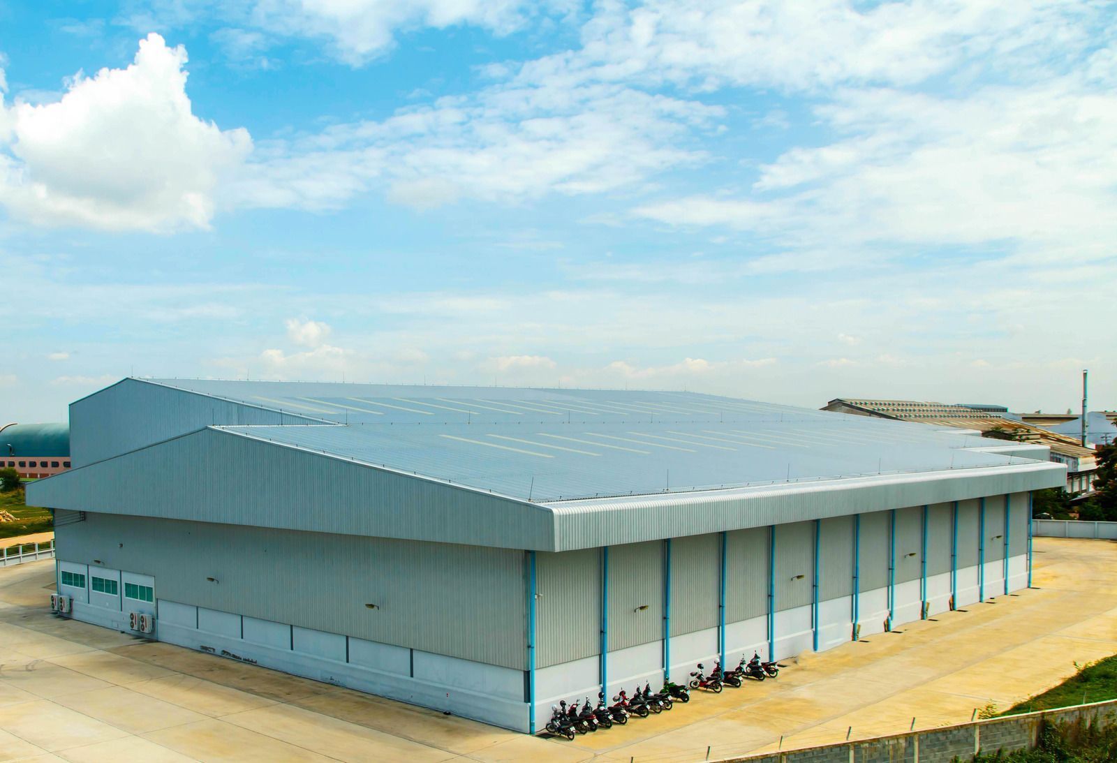 Large industrial warehouse with a blue metal roof and exterior. Sunny day.