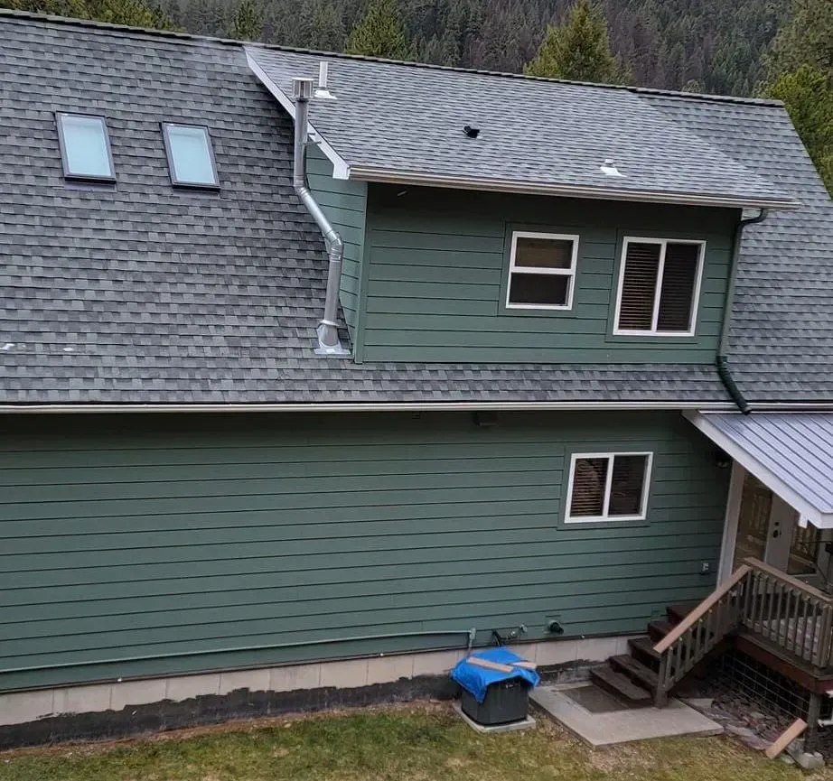 House with brown roof and two-car garage, ladder against the roof, set in a grassy yard.