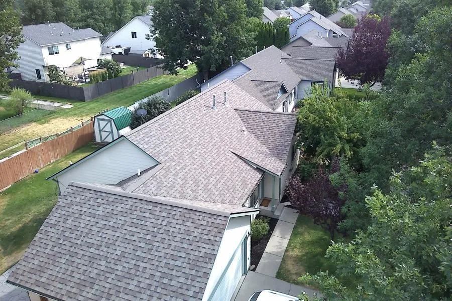Aerial view of suburban homes with gray roofs and trees lining the backyards.