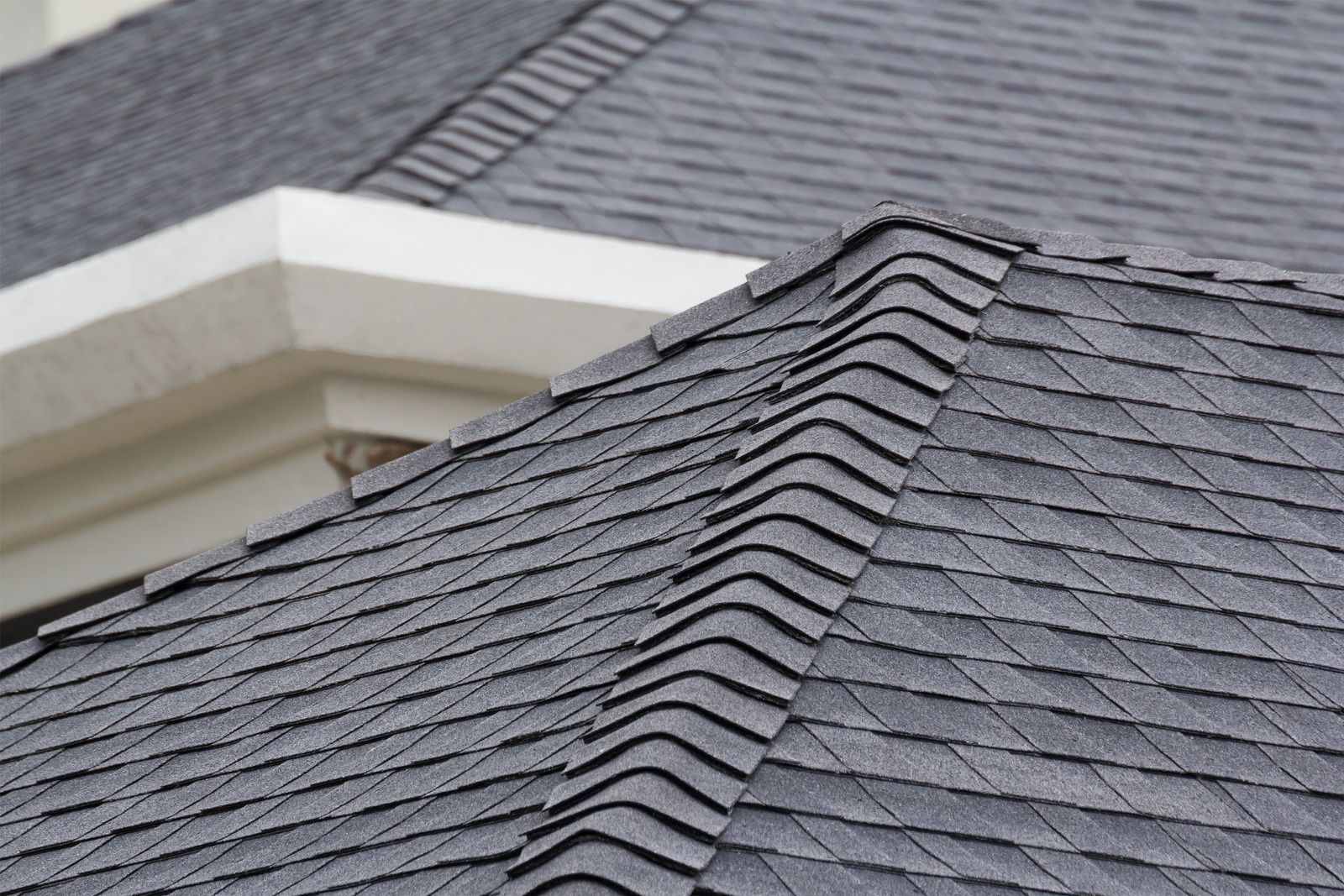 Close-up of a gray shingled roof with a detailed ridge and architectural trim.