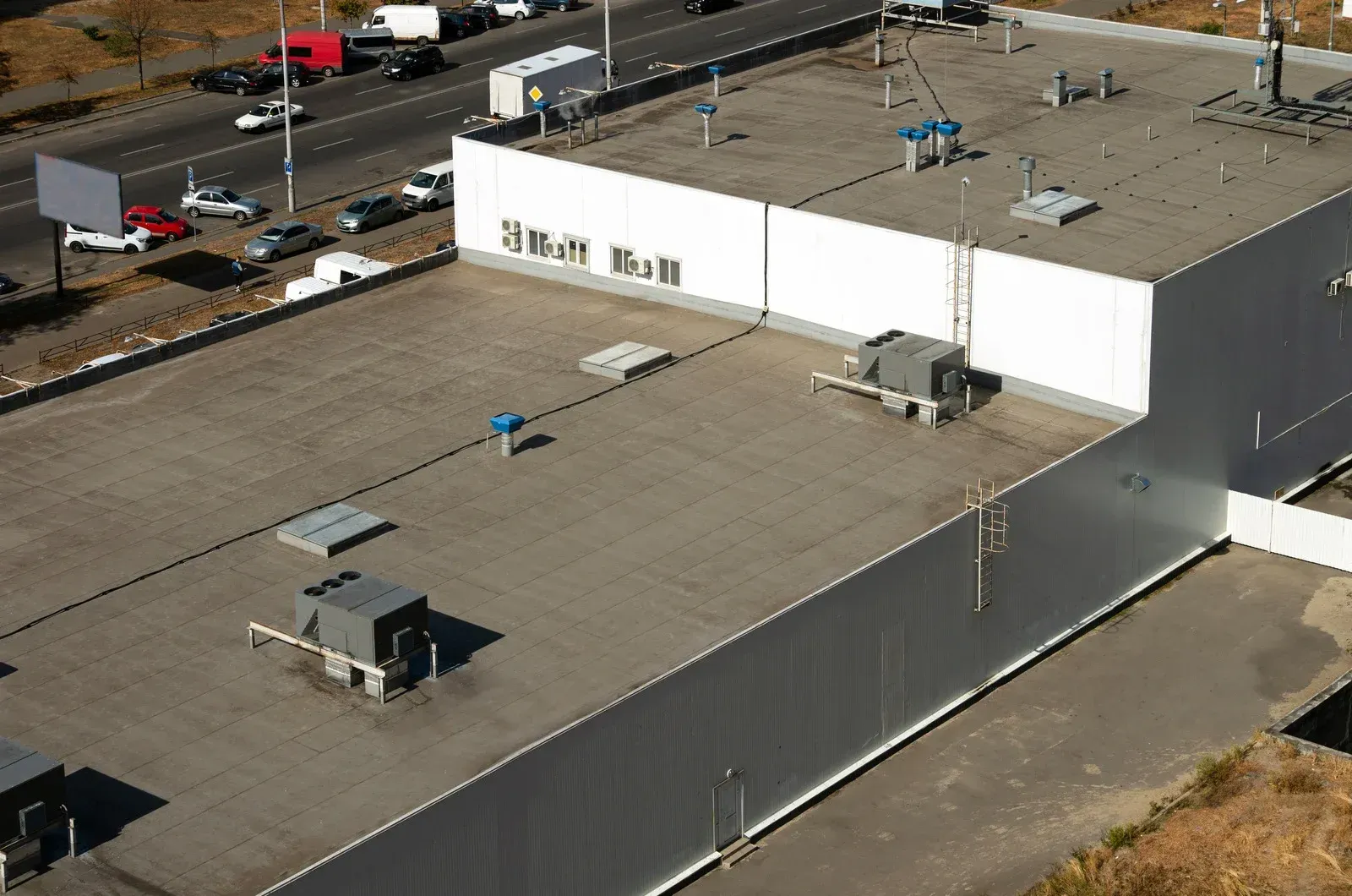 Aerial view of flat white industrial buildings with rooftop HVAC units and a parking lot nearby.