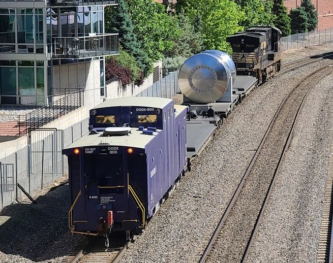 Freight train hauling tank cars curves past a glass building on adjacent tracks