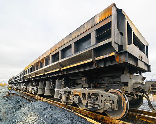 Derailment of a long freight railcar on tracks, with the undercarriage and wheels exposed, in a gravel rail yard