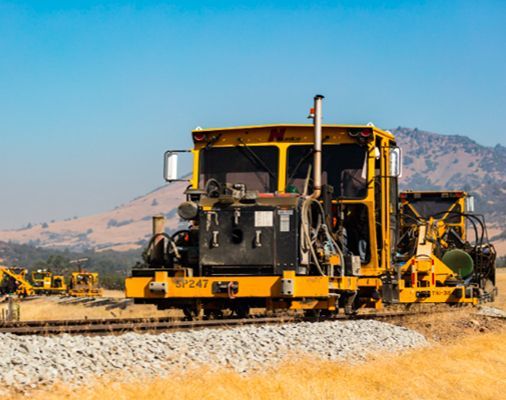 Yellow rail maintenance machine on tracks in a dry desert landscape with mountains in the background