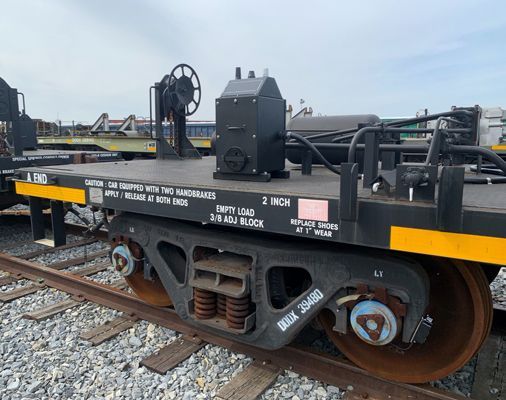 Close-up of a black railcar wheel and machinery on gravel tracks in a rail yard