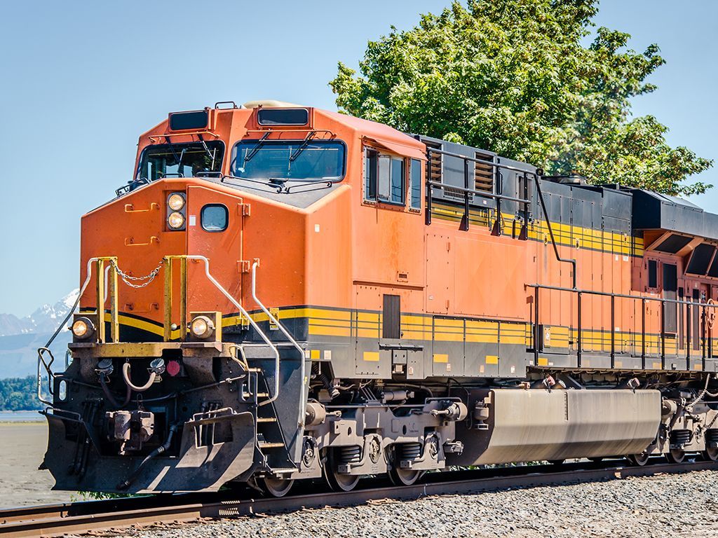 Orange freight locomotive on tracks under a blue sky, with trees in the background