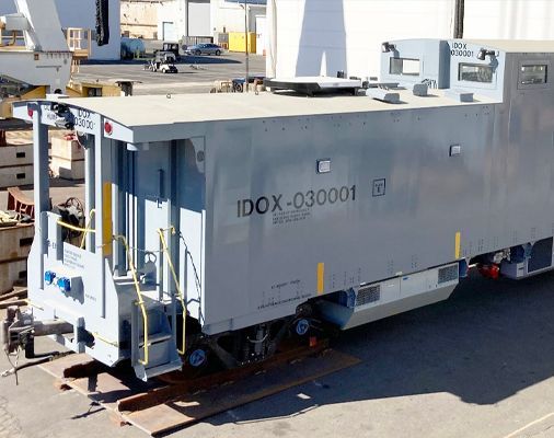 White industrial utility vehicle labeled “IDOX-030001” parked in a lot, with ladders and equipment visible.
