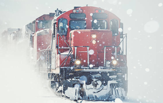 Red locomotive pushing through heavy snowfall on a snowy track