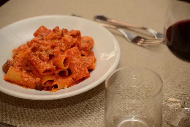 Un piatto di pasta accanto a un bicchiere di vino su un tavolo.