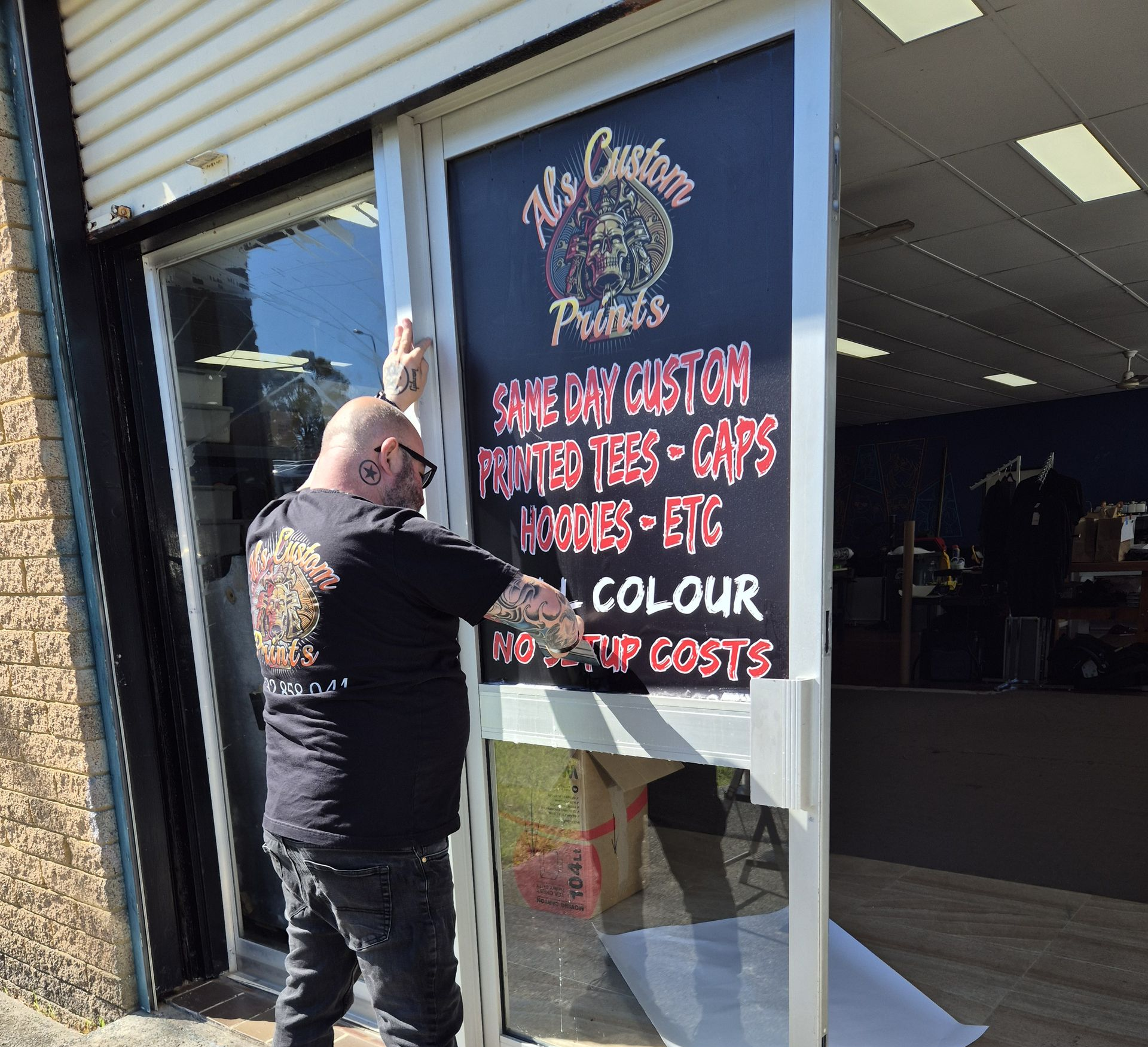 Man applying vinyl lettering to a storefront window — Al's Custom Prints in Wyong, NSW
