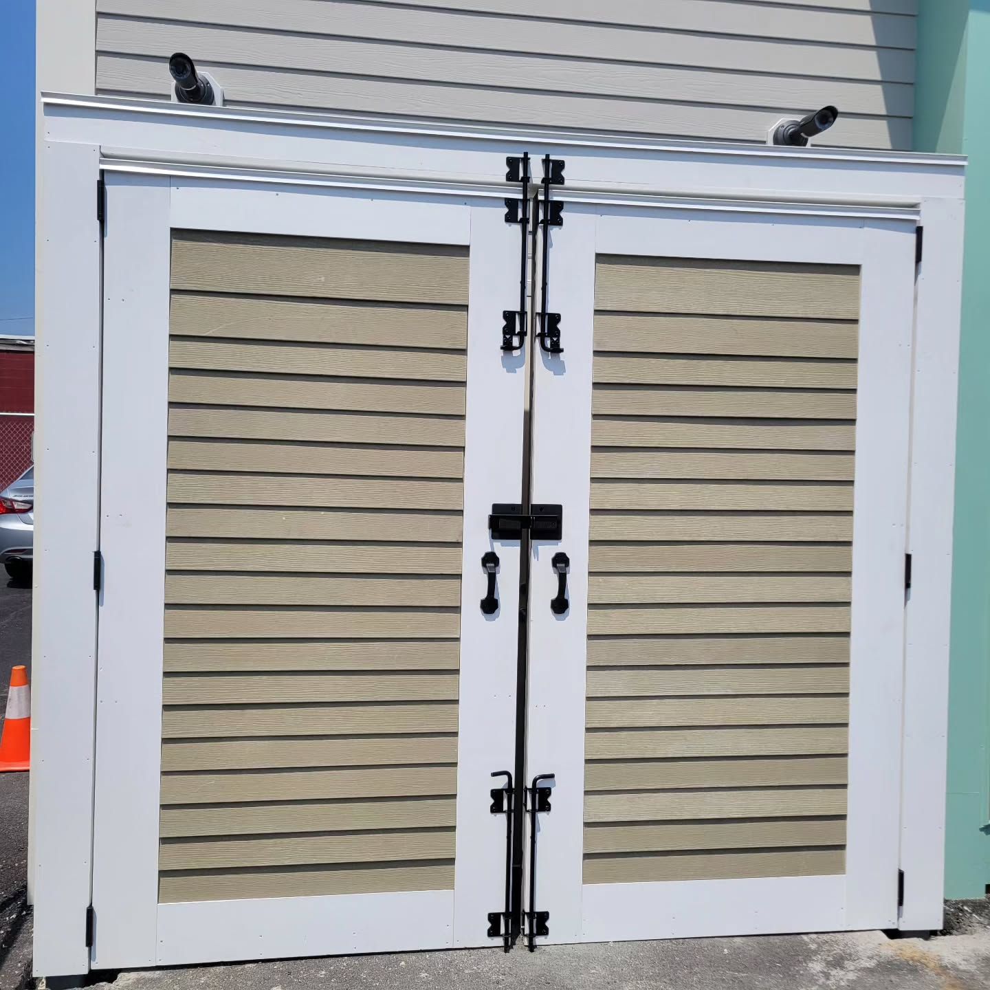 White-framed double doors with beige horizontal slats and black hardware against a light-colored building.