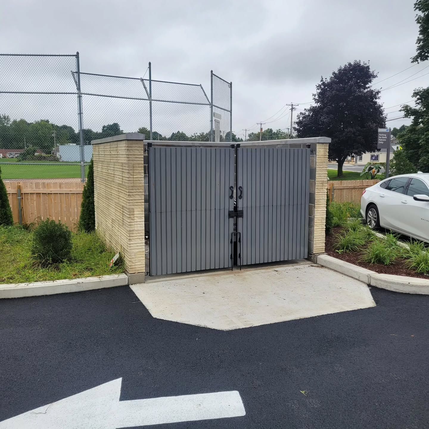 Gray trash enclosure with concrete pad and arrow on pavement.