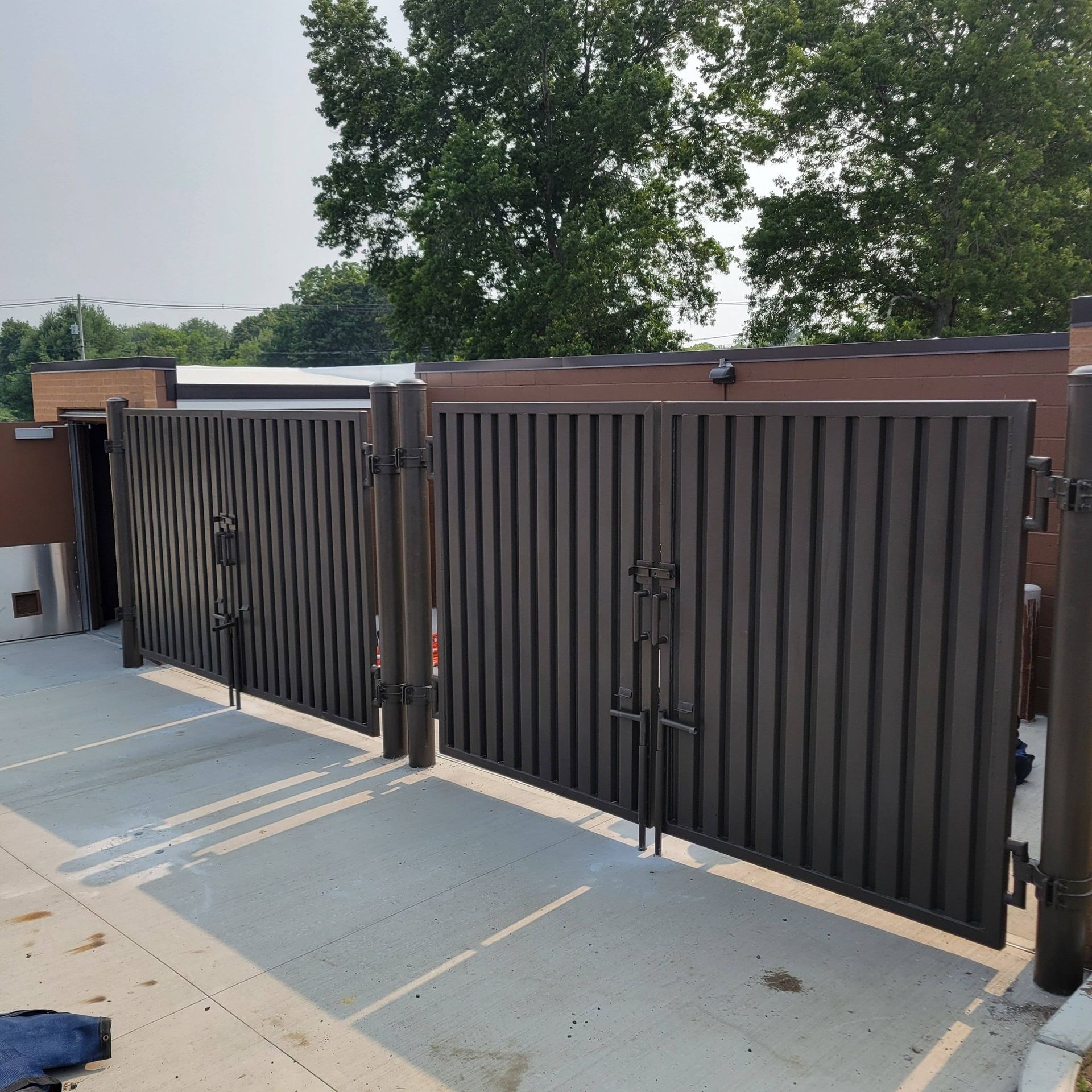 Closed dark brown metal gate with vertical slats, on a concrete patio.