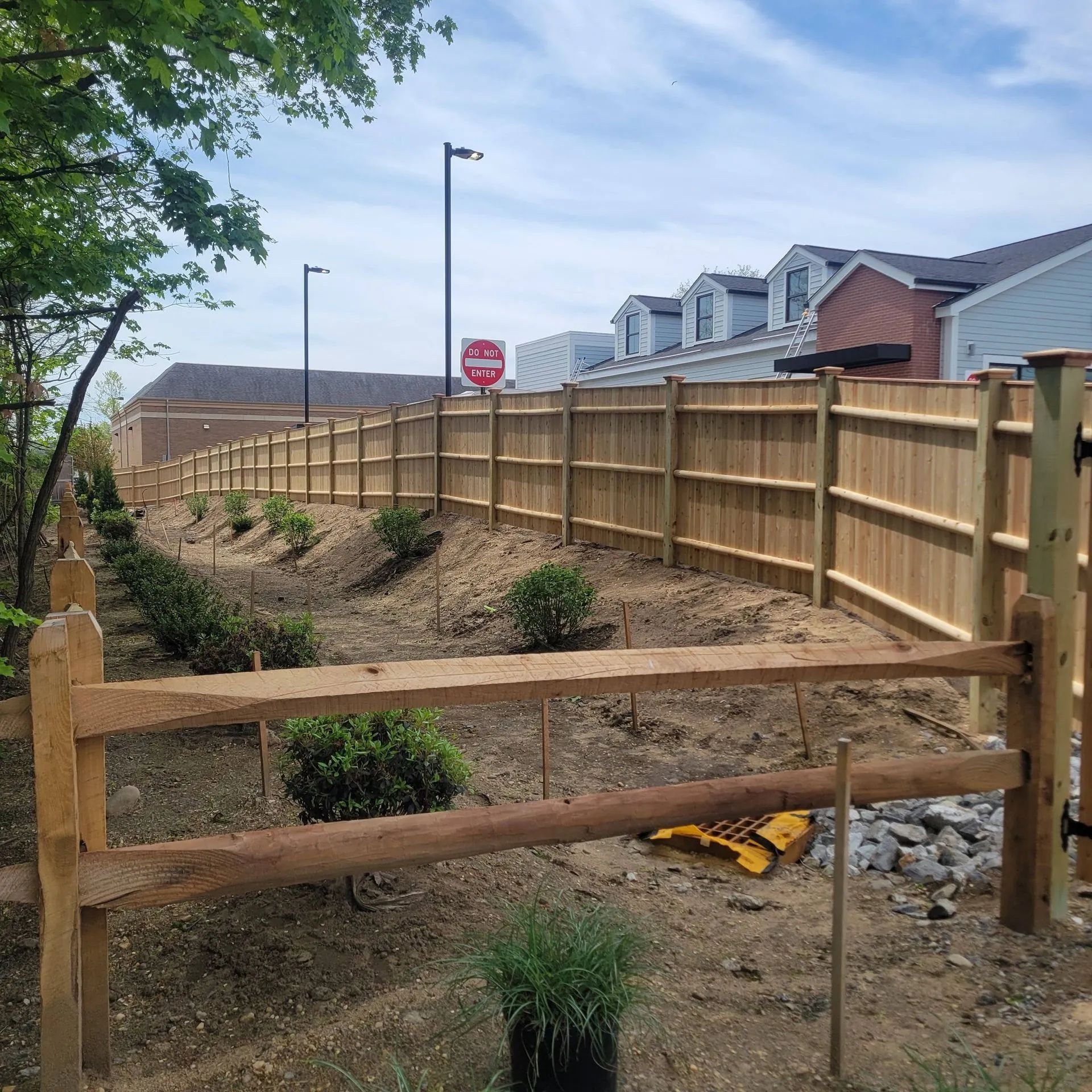 Wooden fence along a dirt slope in a suburban neighborhood, with a stop sign in the distance.