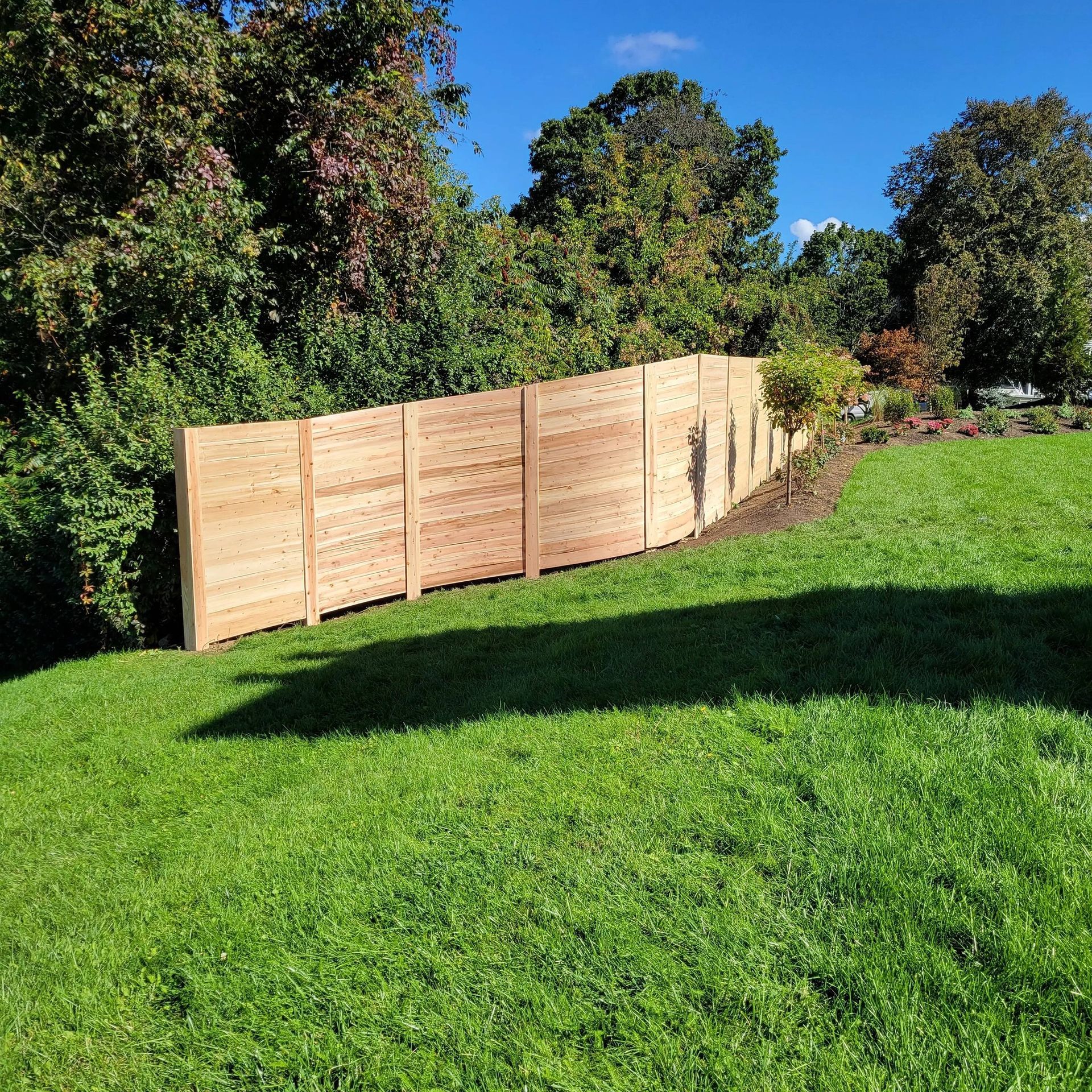 A wooden fence on a grassy hill; trees in the background under a blue sky.