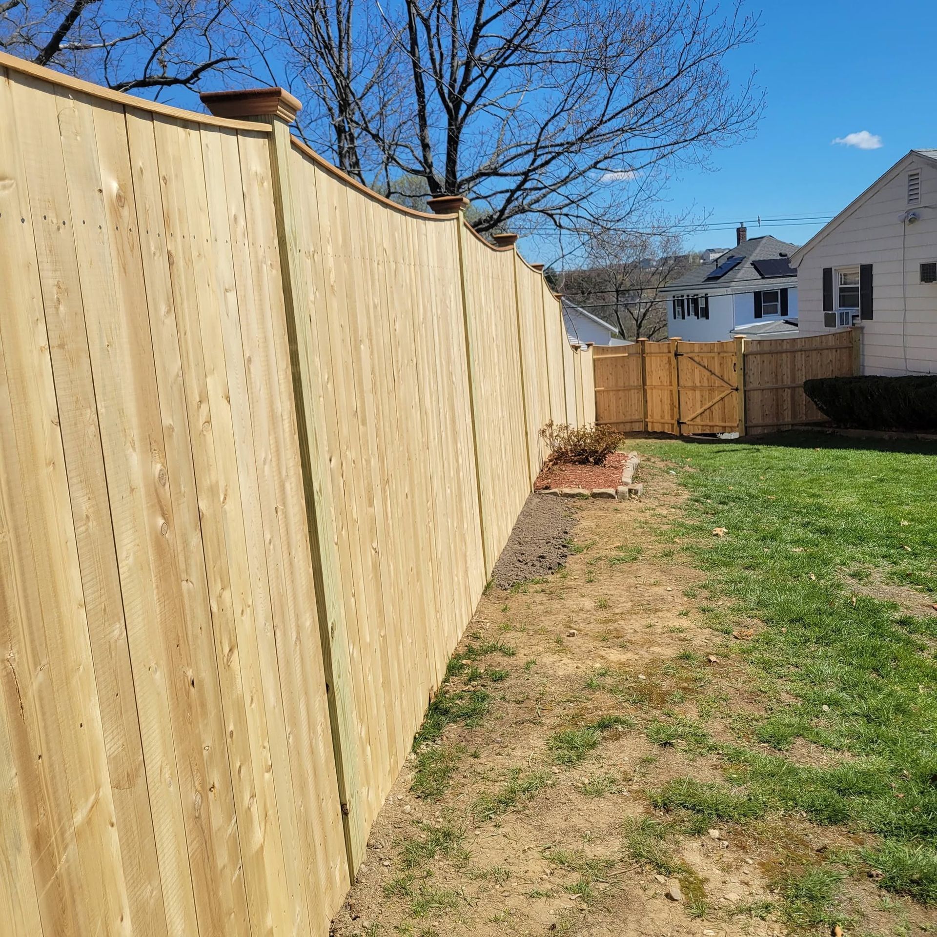 Wooden privacy fence along a grassy backyard beside a house under a clear blue sky