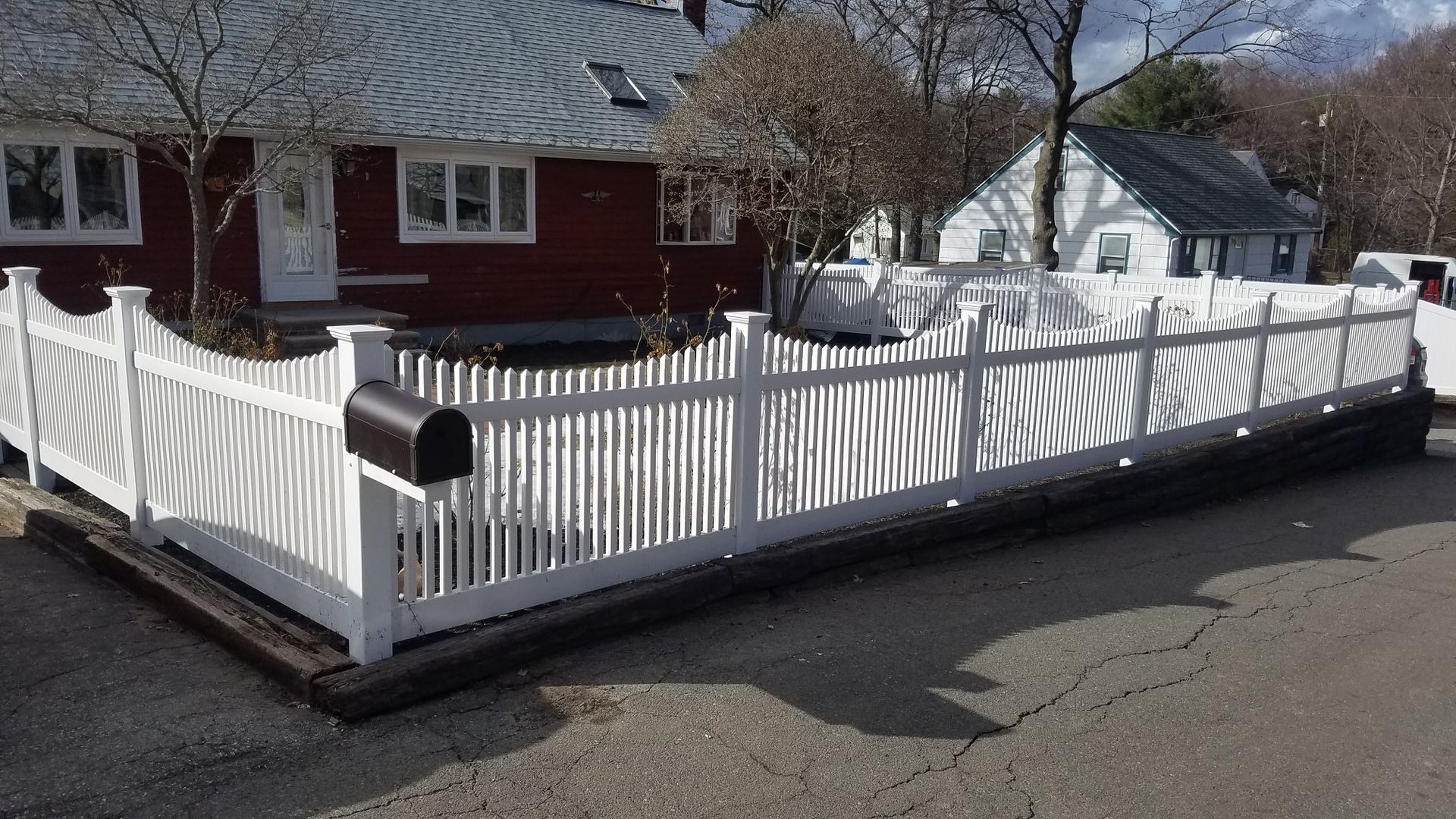 White picket fence in front of a red house, with a black mailbox.