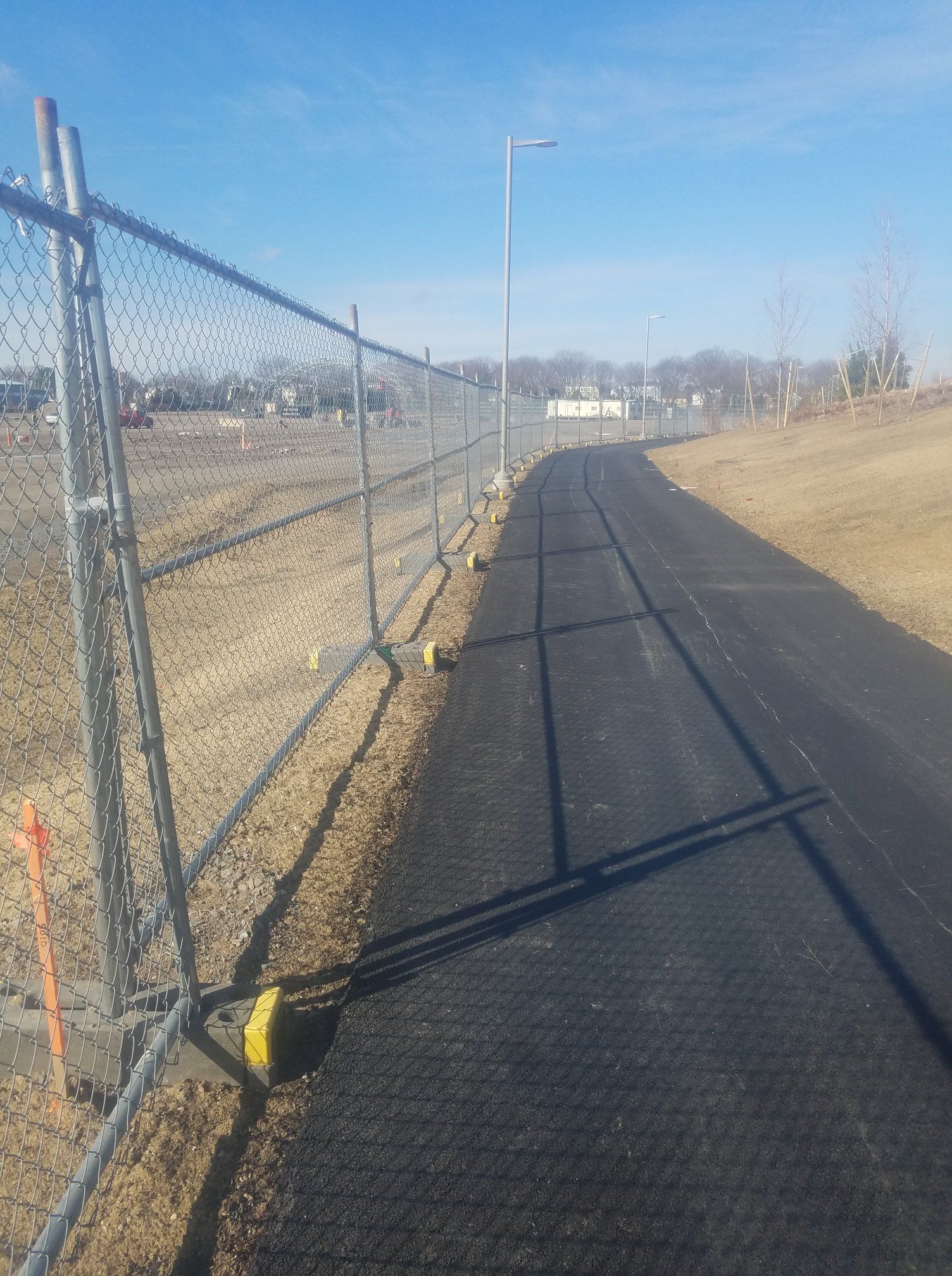 Chain link fence beside a paved path on a sunny day.