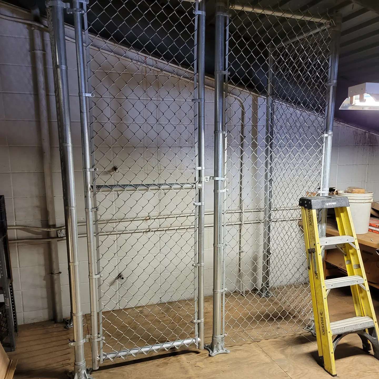 Chain link fence sections with a yellow ladder in an indoor setting.