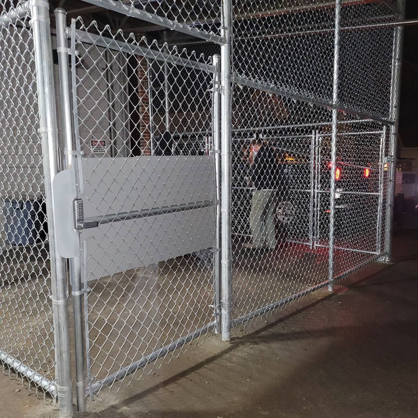 Chain-link fence enclosure with a metal gate. Industrial setting, exterior.