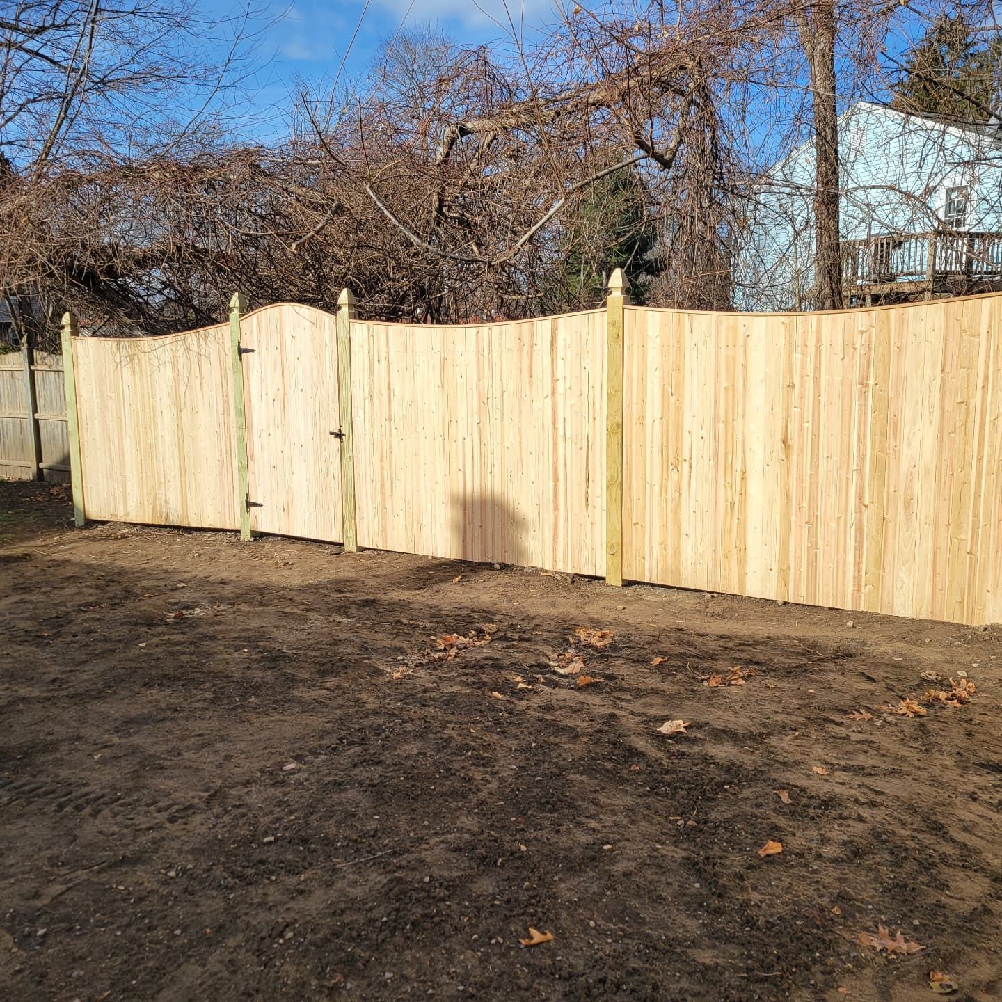 Wooden fence in a yard with a gate, trees and a house in the background.