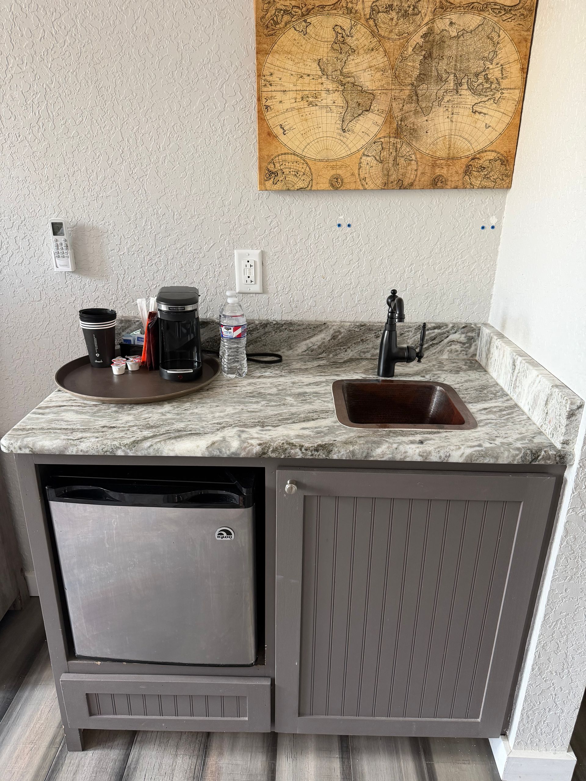 Small kitchenette with mini fridge, granite counter, sink, coffee maker, and wall art.