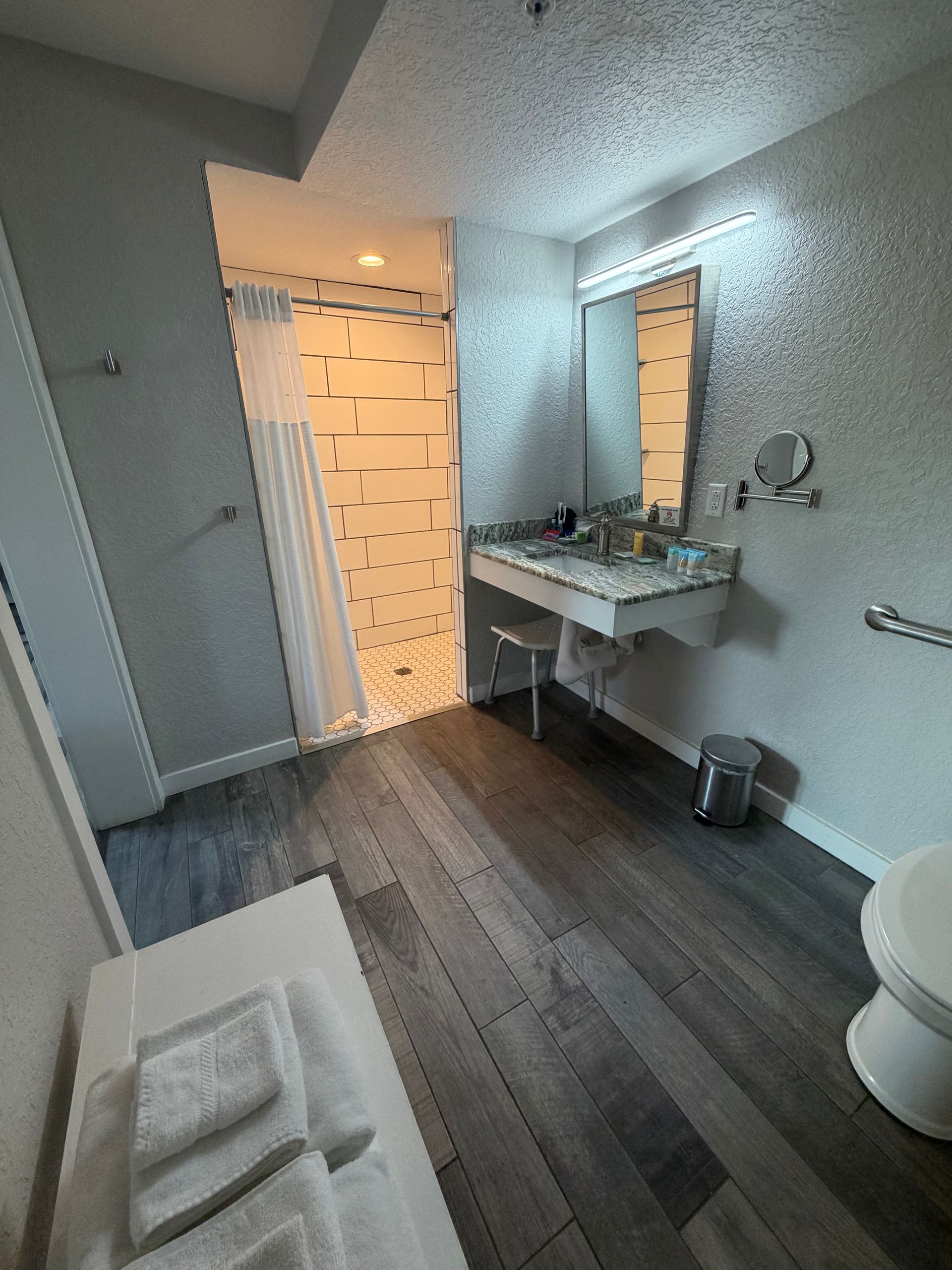 Modern bathroom with gray tile floor, white sink vanity, mirror, shower, and toilet in a bright room
