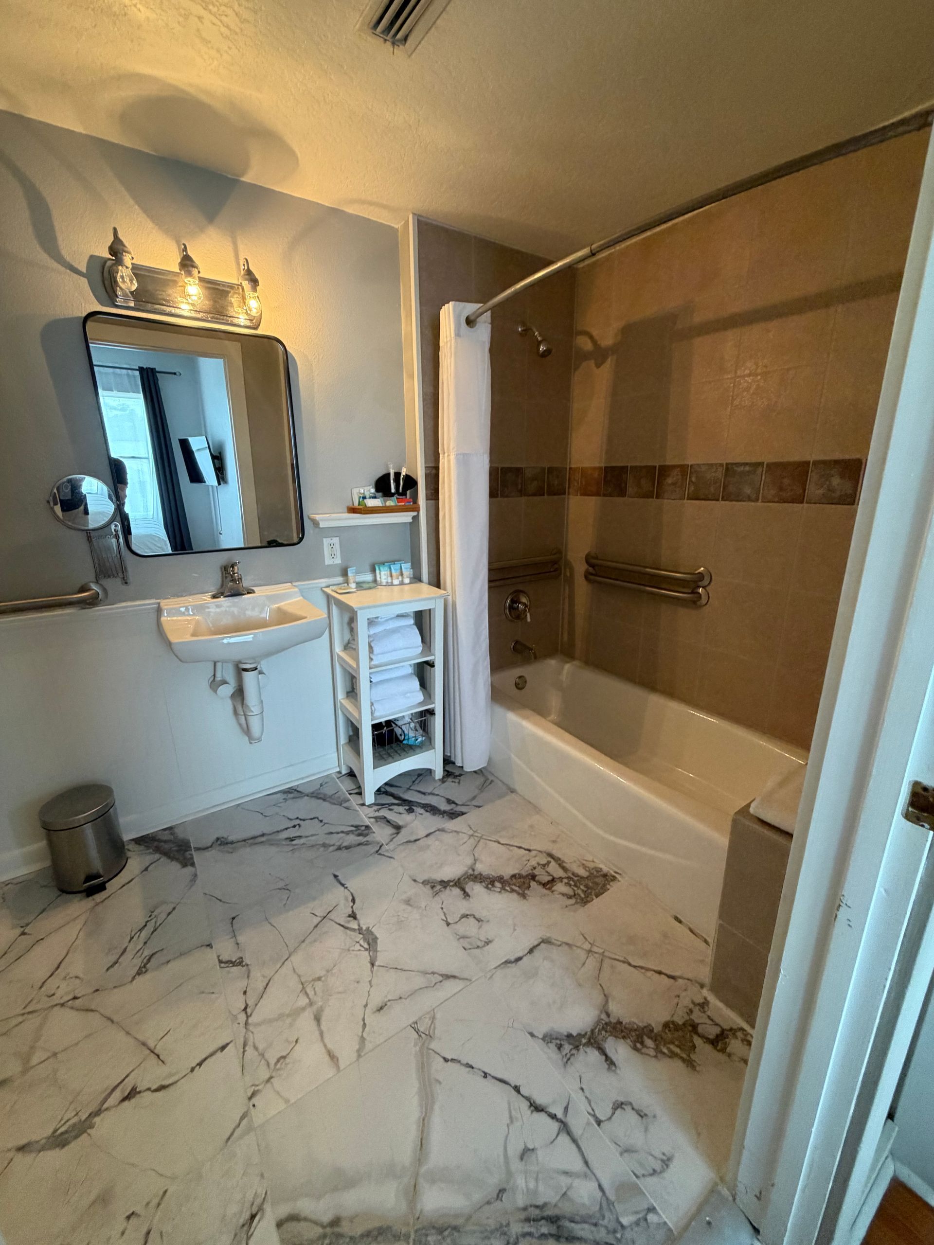 Bathroom with marble tile floor, vanity mirror, sink, and beige tub/shower surround