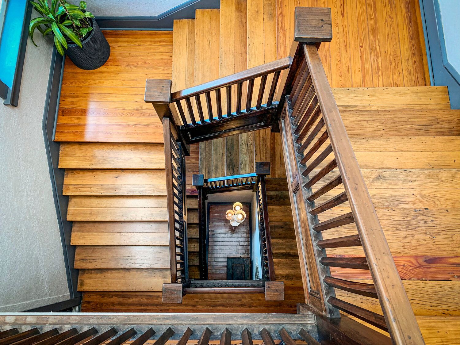 Wooden staircase spiraling down around a central open shaft with a potted plant on the landing.