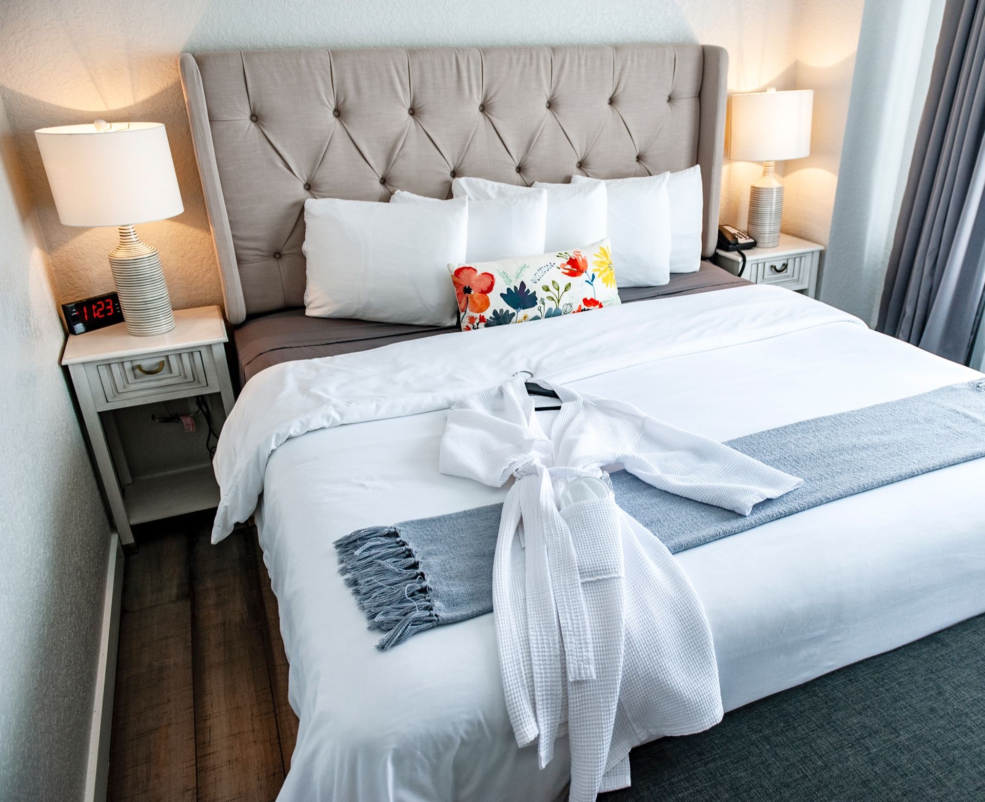 Bright bedroom with tufted gray headboard, white bedding, and bedside lamps