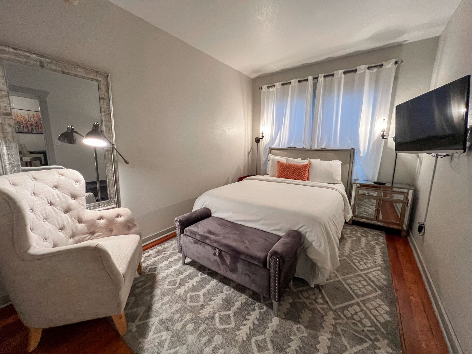 A bedroom with a bed , chair , television and mirror.