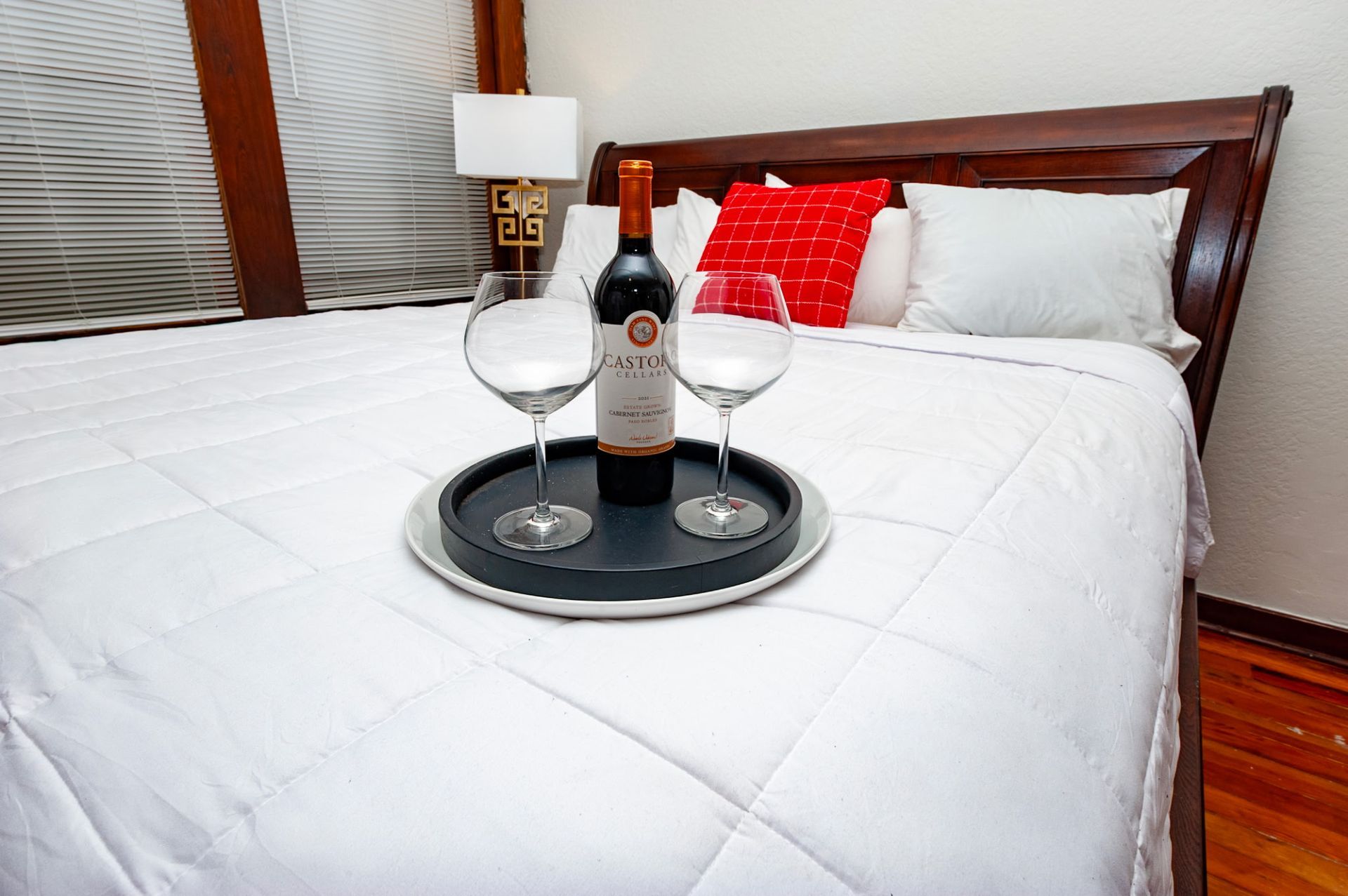 Breakfast tray on a bed with wine bottle and two glasses in a cozy hotel room